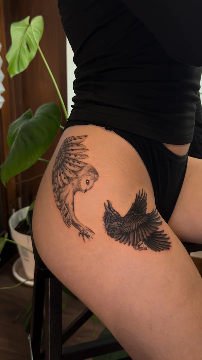 Tatuagem de uma coruja e um corvo em voo na coxa.